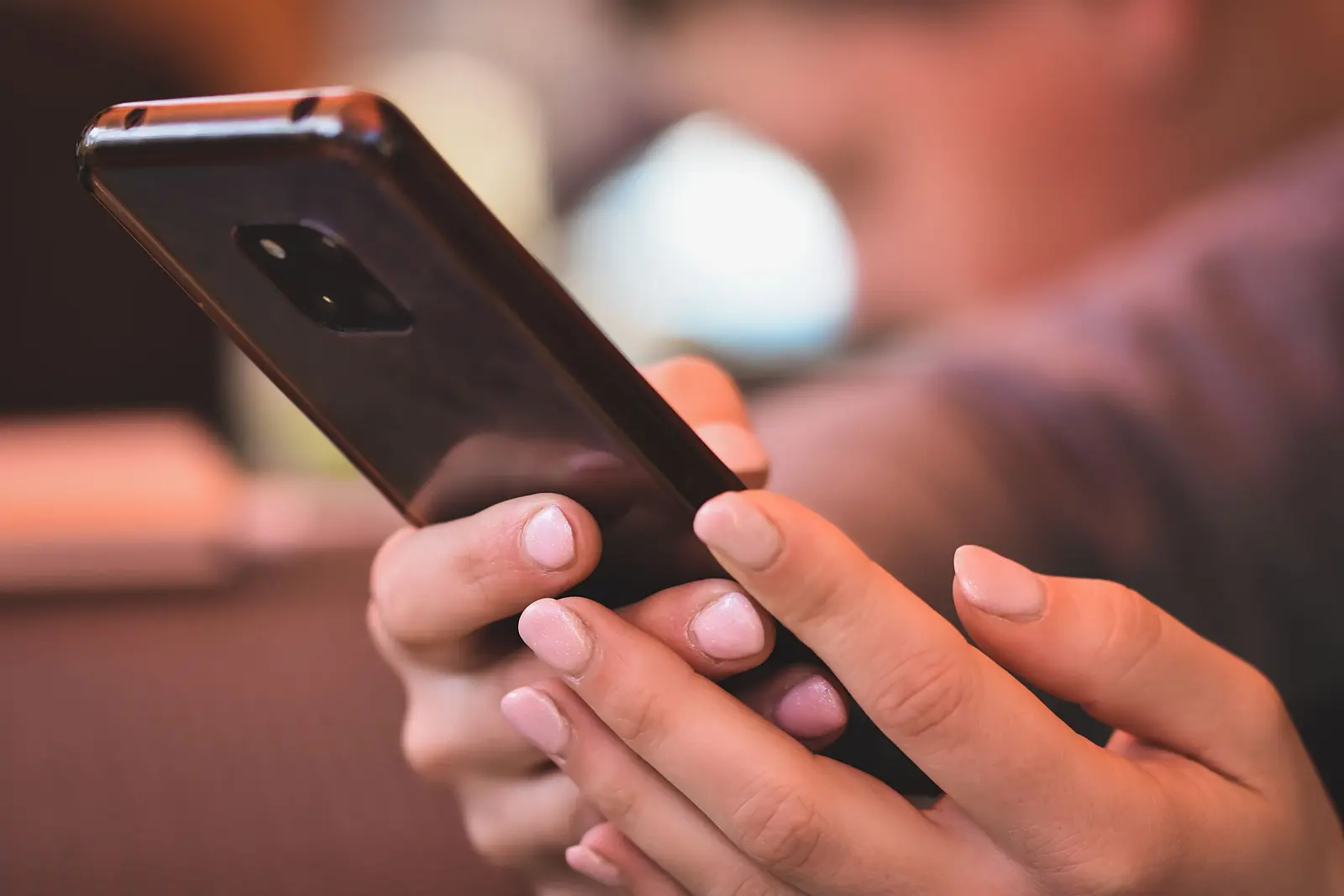Zwei Hände halten ein Smartphone vor einem warm beleuchteten, unscharfen Raum