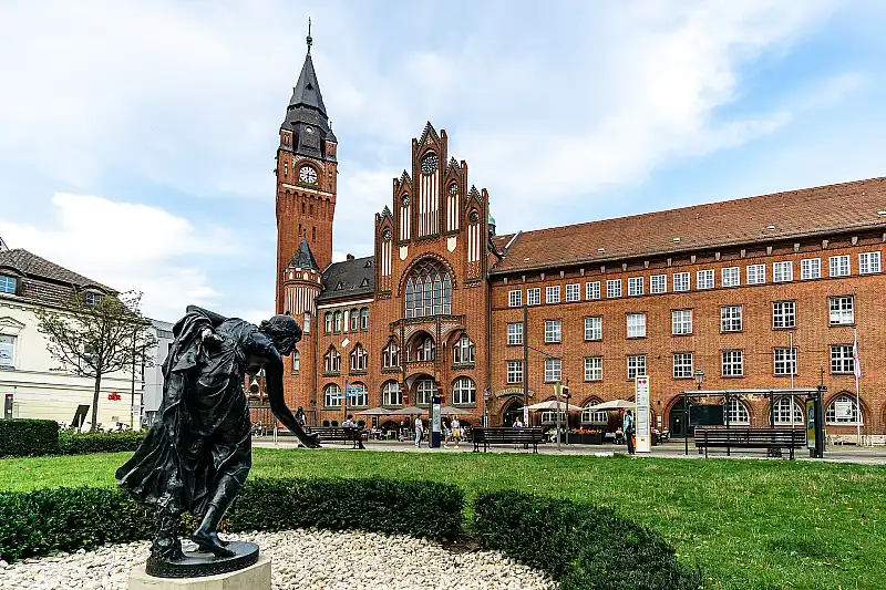 Das Rathaus Köpenick, ein roter Backsteinbau mit Turm, davor eine Bronzefigur auf dem Rasen