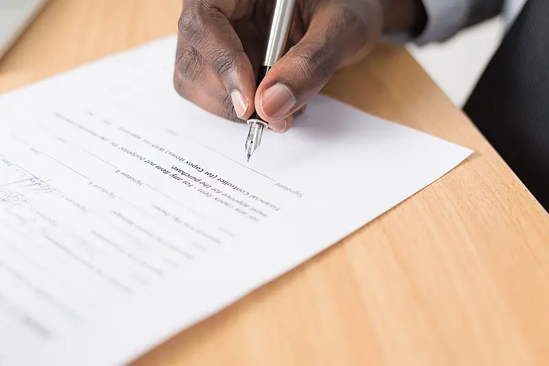 Eine Hand setzt mit einem Füller die Unterschrift unter ein Schriftstück, der Text auf dem Papier ist nicht lesbar